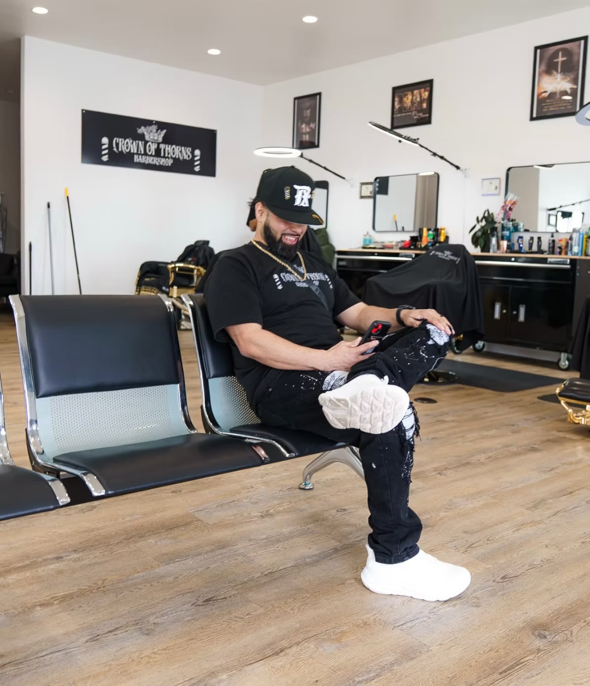 Founder Michael Reynosa seated on the black waiting chairs inside Crown of Thorns Barbershop